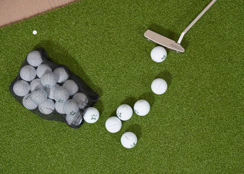 Overhead shot of golf balls, putter, and bag on a putting green turf.